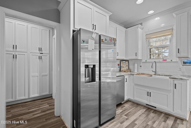 kitchen with stainless steel appliances, light stone countertops, light hardwood / wood-style flooring, and white cabinets