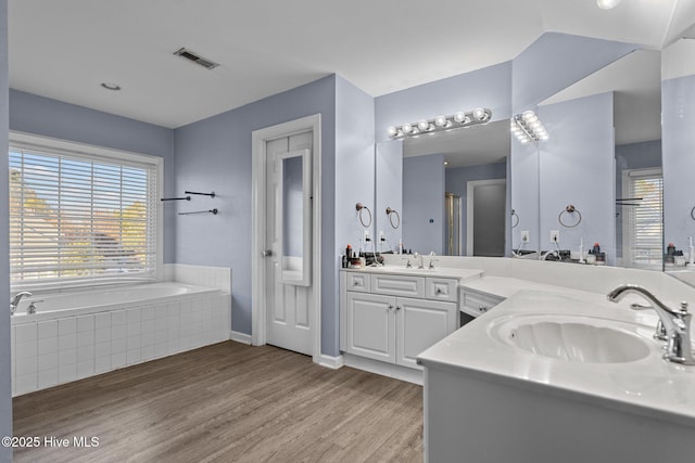 bathroom featuring a relaxing tiled tub, hardwood / wood-style floors, vanity, and plenty of natural light