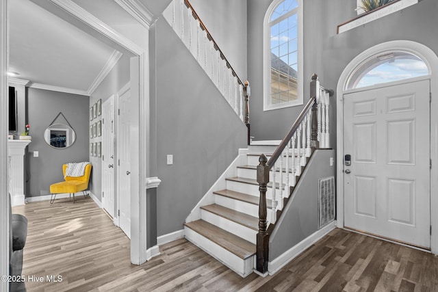 entryway with hardwood / wood-style flooring, ornamental molding, and a high ceiling