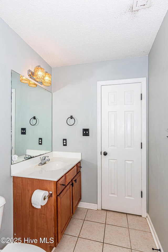 bathroom featuring a textured ceiling, baseboards, toilet, vanity, and tile patterned flooring