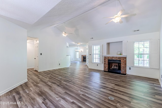 unfurnished living room featuring a brick fireplace, a ceiling fan, visible vents, baseboards, and dark wood finished floors