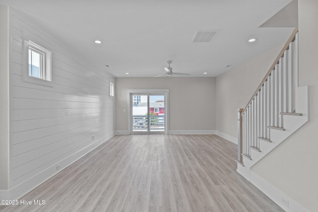 unfurnished living room with ceiling fan, wooden walls, and light hardwood / wood-style floors