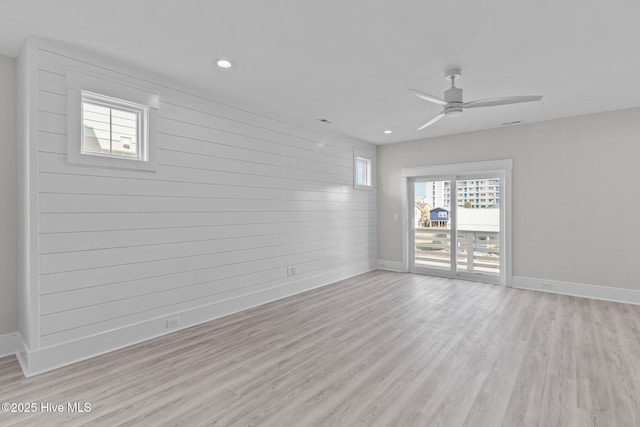 unfurnished room with wood walls, ceiling fan, and light hardwood / wood-style flooring