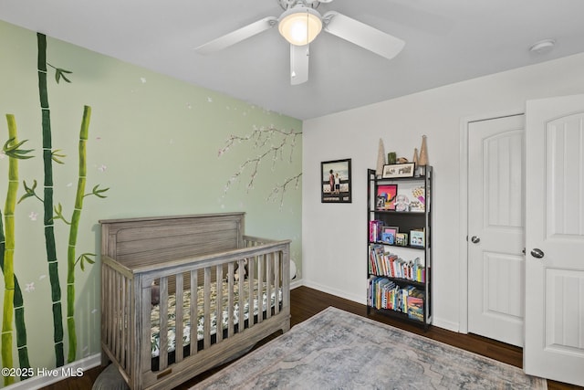 bedroom with dark hardwood / wood-style flooring, a crib, and ceiling fan