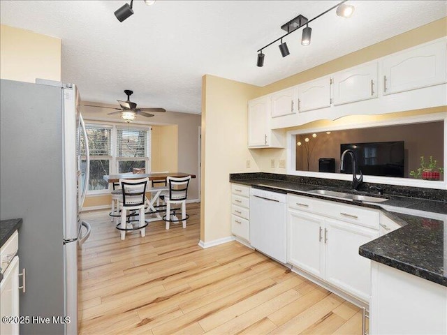 kitchen featuring sink, stainless steel fridge, dishwasher, white cabinetry, and dark stone countertops