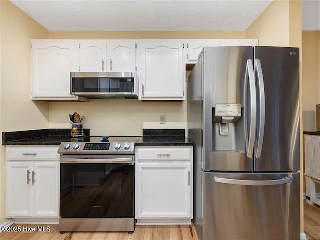 kitchen featuring appliances with stainless steel finishes, white cabinetry, dark stone countertops, light hardwood / wood-style floors, and a textured ceiling