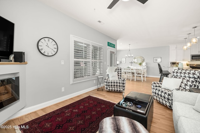 living room with light wood finished floors, baseboards, visible vents, and a glass covered fireplace