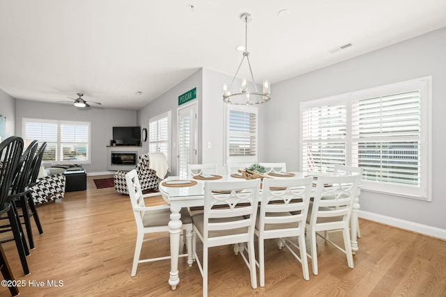 dining room with light wood-style flooring, a glass covered fireplace, and a wealth of natural light