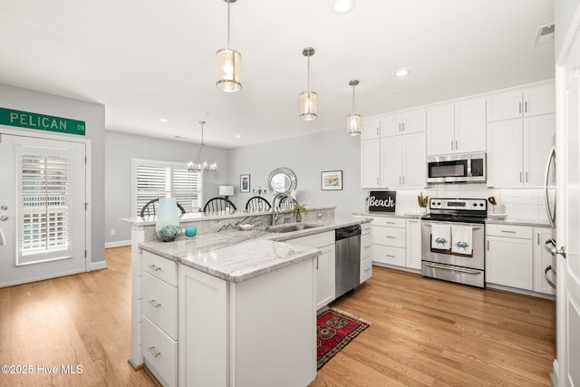 kitchen featuring a sink, appliances with stainless steel finishes, light wood-type flooring, tasteful backsplash, and a center island with sink