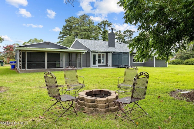 back of house with a lawn, a sunroom, and an outdoor fire pit