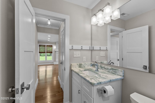 bathroom featuring wood-type flooring, ornamental molding, vanity, and toilet