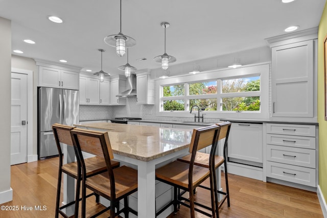 kitchen featuring a breakfast bar, stainless steel refrigerator, decorative light fixtures, a center island, and wall chimney range hood