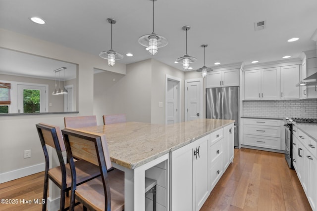 kitchen with appliances with stainless steel finishes, a kitchen bar, decorative light fixtures, and white cabinets