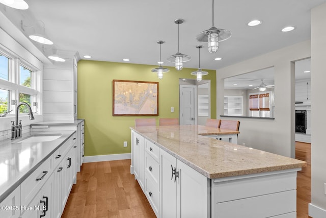 kitchen with sink, white cabinetry, a center island, hanging light fixtures, and light stone countertops