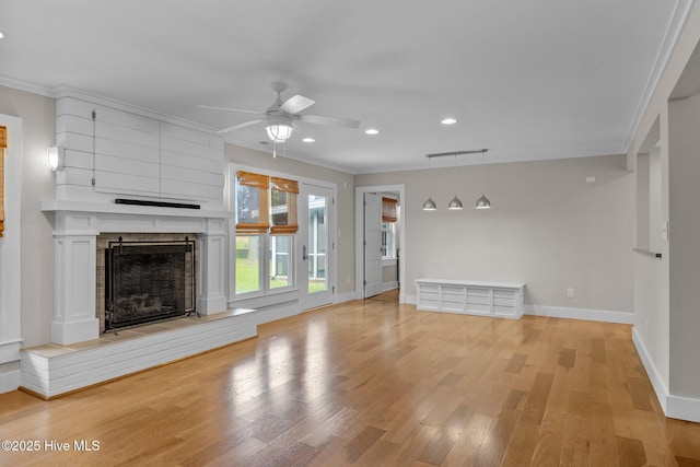 unfurnished living room with crown molding, a large fireplace, ceiling fan, and light wood-type flooring