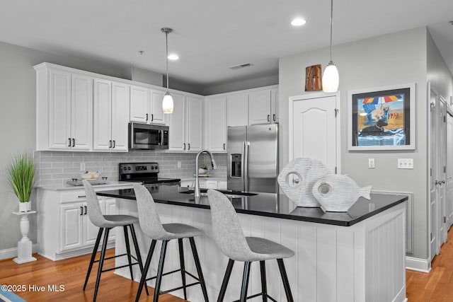 kitchen with white cabinets, light wood-type flooring, appliances with stainless steel finishes, and a kitchen island with sink