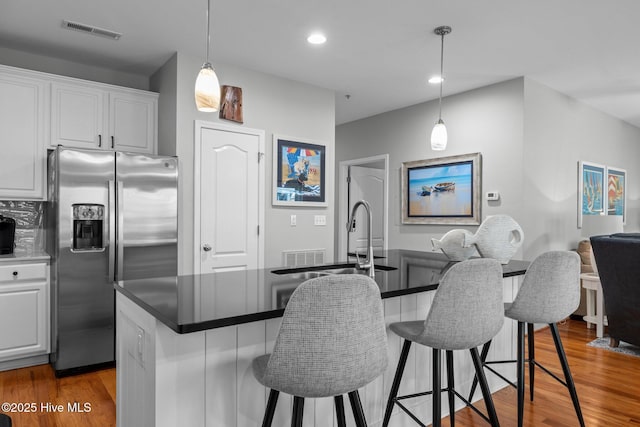 kitchen featuring white cabinets, stainless steel refrigerator with ice dispenser, and a kitchen island with sink