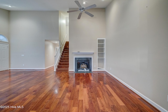 unfurnished living room with ceiling fan, wood-type flooring, and a high ceiling