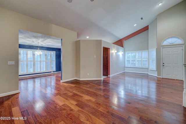 unfurnished living room with wood-type flooring, ceiling fan with notable chandelier, and high vaulted ceiling