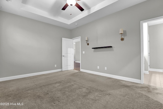 interior space with ceiling fan, a tray ceiling, and light carpet