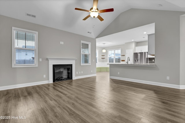 unfurnished living room with wood-type flooring, high vaulted ceiling, sink, and ceiling fan