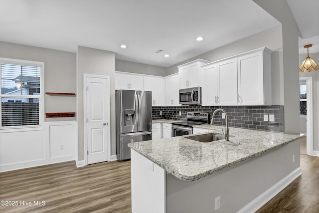 kitchen featuring sink, white cabinetry, kitchen peninsula, stainless steel appliances, and light stone countertops