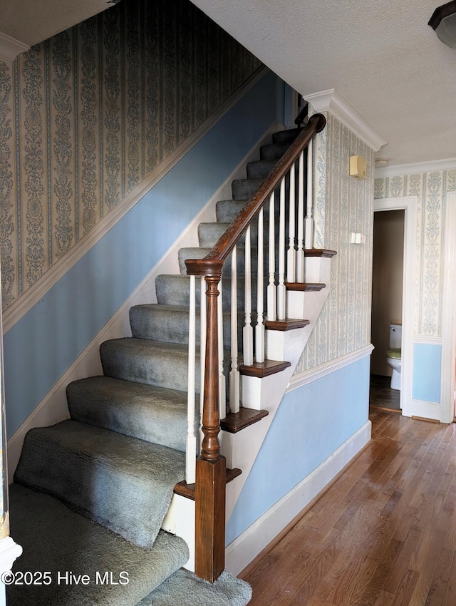 stairway featuring crown molding, wood-type flooring, and a textured ceiling