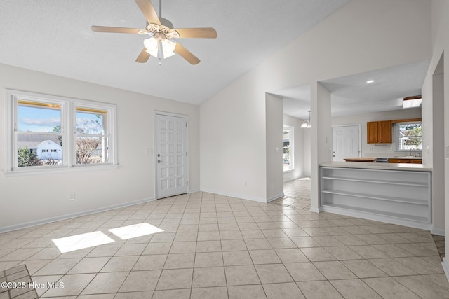 unfurnished living room featuring a wealth of natural light, lofted ceiling, light tile patterned flooring, and baseboards