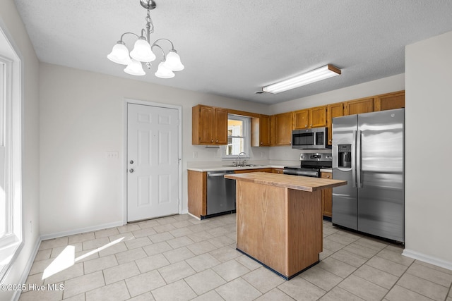 kitchen featuring stainless steel appliances, a sink, hanging light fixtures, wooden counters, and a center island