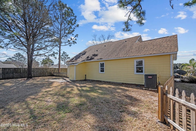 rear view of property with central AC unit, a lawn, a shingled roof, and fence private yard