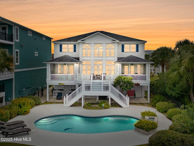 57 Craven St, Ocean Isle Beach, NC 28469 - back of house at dusk featuring a patio, an outdoor pool, a shingled roof, and stairway