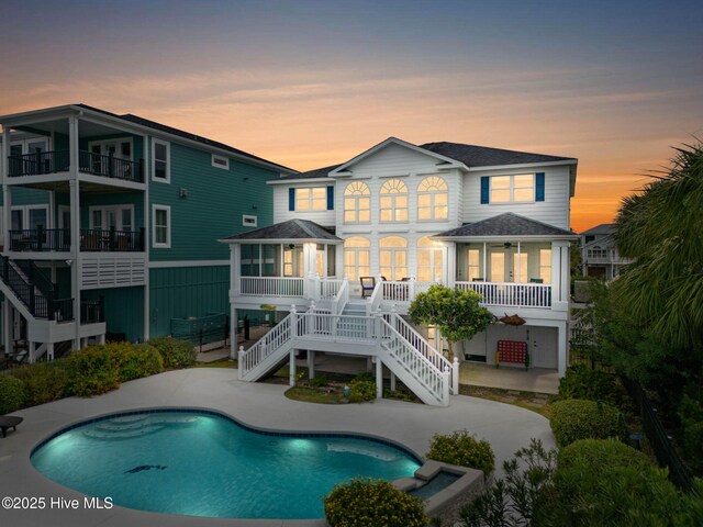 57 Craven St, Ocean Isle Beach, NC 28469 - back of property at dusk with stairs, an outdoor pool, a patio area, and roof with shingles