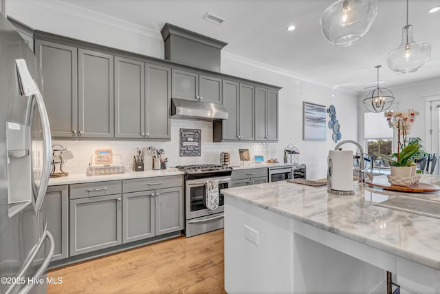 kitchen with light stone counters, gray cabinets, ornamental molding, and appliances with stainless steel finishes