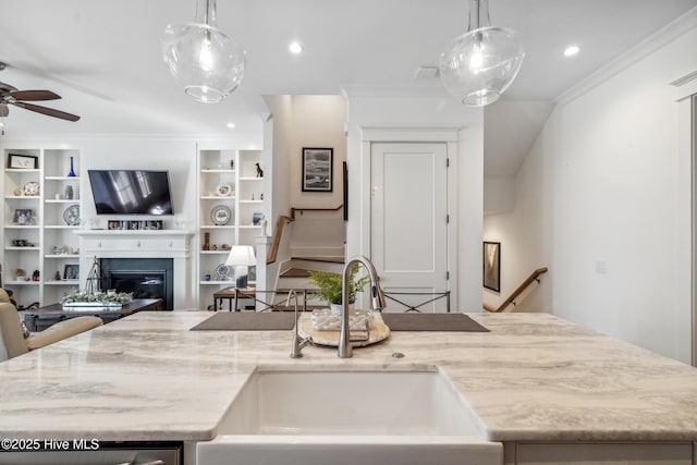 kitchen with crown molding, light stone countertops, sink, and decorative light fixtures