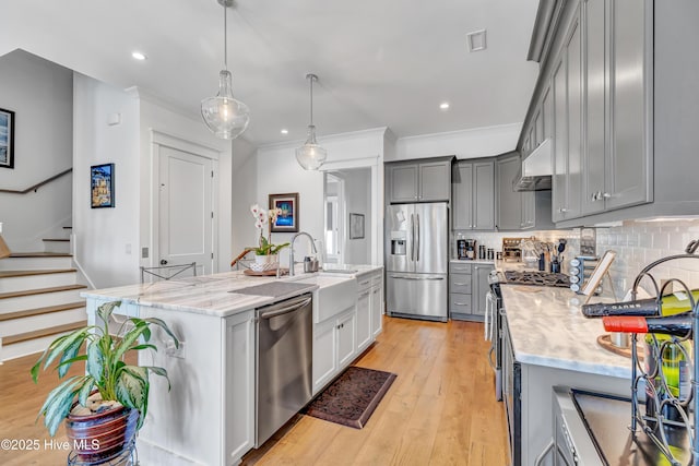 kitchen with crown molding, a kitchen island with sink, stainless steel appliances, decorative backsplash, and decorative light fixtures