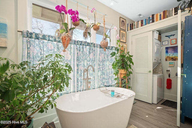 530 Contentnea Ave, New Bern, NC 28560 - bathroom featuring stacked washer and clothes dryer, a freestanding bath, wood finished floors, and plenty of natural light