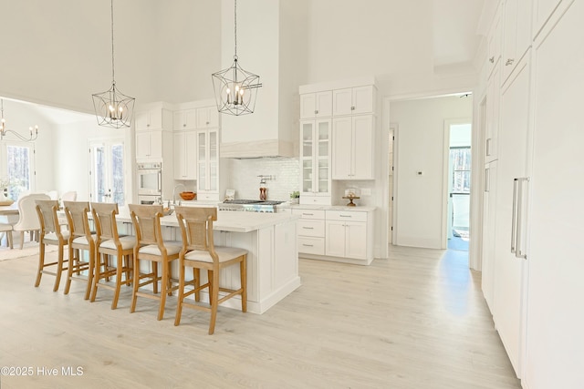 kitchen featuring white cabinets, an island with sink, glass insert cabinets, light countertops, and a chandelier