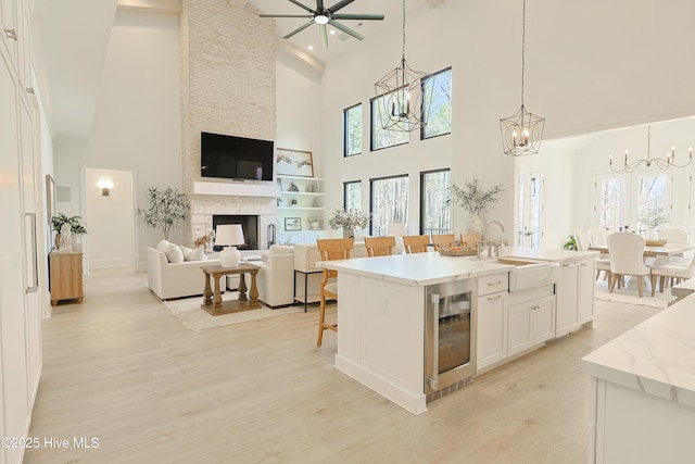 kitchen with wine cooler, a kitchen island with sink, white cabinets, open floor plan, and decorative light fixtures