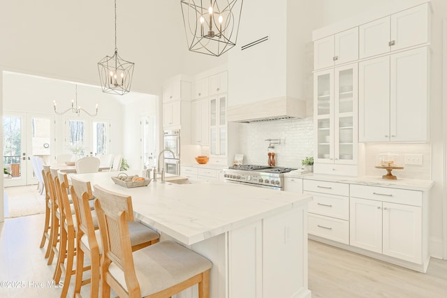 kitchen with a chandelier, a kitchen island with sink, decorative light fixtures, stove, and glass insert cabinets