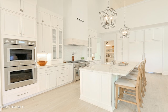 kitchen with stainless steel appliances, glass insert cabinets, a center island with sink, and white cabinets