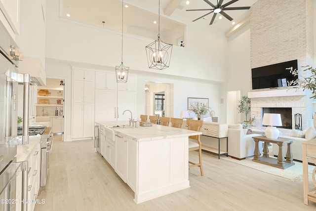 kitchen with light stone counters, open floor plan, a kitchen island with sink, white cabinetry, and pendant lighting