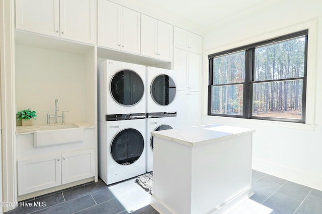 laundry area with cabinet space, baseboards, stacked washing maching and dryer, dark tile patterned floors, and a sink