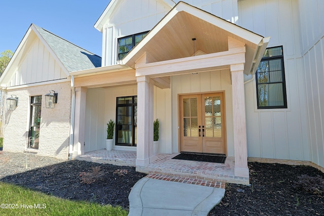 property entrance featuring roof with shingles, french doors, board and batten siding, and brick siding