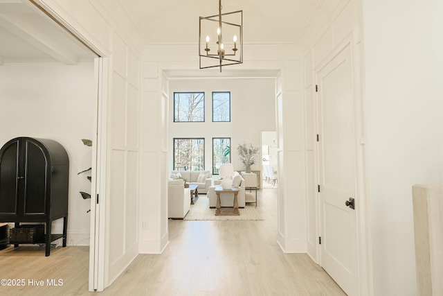 hall with light wood-style floors, a chandelier, crown molding, and a towering ceiling