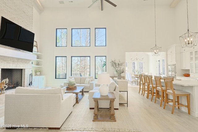 living room with a fireplace, light wood finished floors, and ceiling fan with notable chandelier