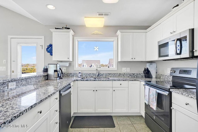 kitchen featuring appliances with stainless steel finishes, light stone countertops, light tile patterned flooring, sink, and white cabinetry