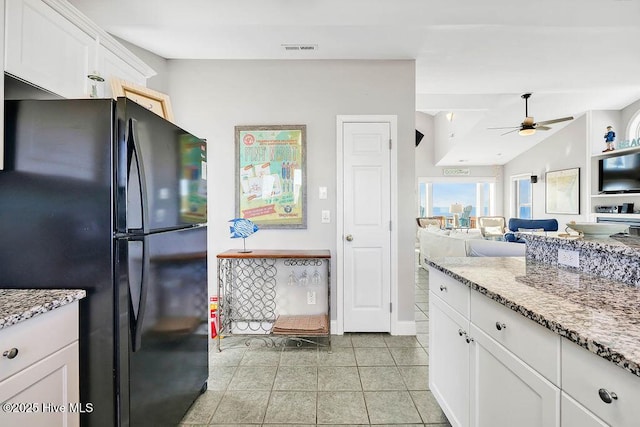 kitchen featuring black refrigerator, light stone countertops, ceiling fan, light tile patterned floors, and white cabinetry