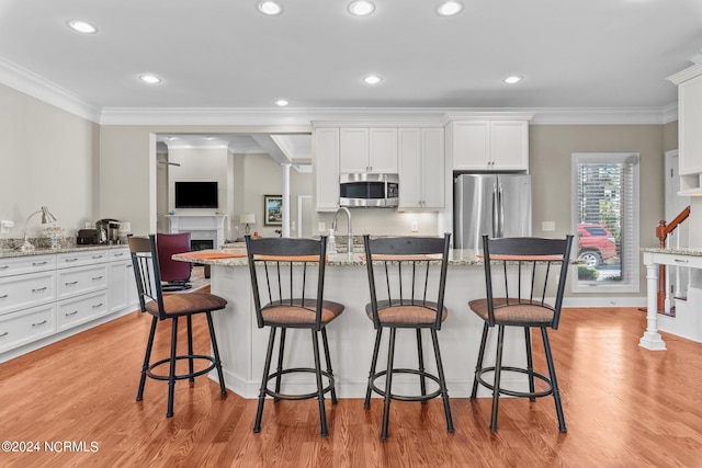 kitchen with appliances with stainless steel finishes, white cabinetry, a breakfast bar area, light stone counters, and a center island with sink