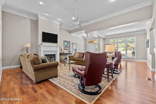 living room featuring a premium fireplace, wood-type flooring, ceiling fan, and crown molding