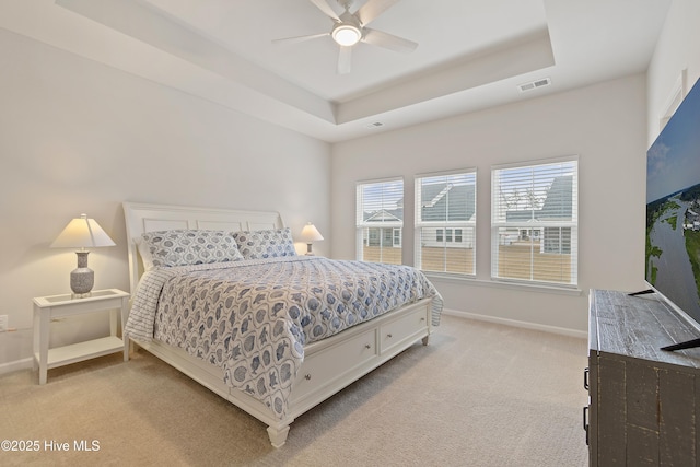 bedroom featuring ceiling fan, a tray ceiling, and light carpet